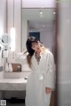 A woman in a white robe standing in front of a mirror.