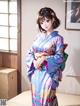 A woman in a blue kimono standing in front of a window.