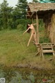 A naked woman standing on a wooden bridge over a river.