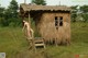 A naked woman standing on a ladder in front of a hut.