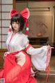 A woman in a red and white kimono sitting on a wooden floor.