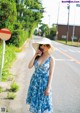 A woman in a blue dress and hat drinking from a cup.