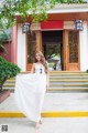 A woman in a white dress standing in front of a building.