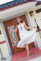 A woman in a white dress standing in front of a door.