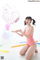 A woman in a pink bathing suit holding a bunch of balloons.