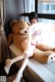 A woman sitting on a window sill next to a teddy bear.