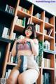 A woman sitting on top of a book shelf holding a book.