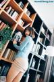 A woman standing in front of a bookshelf holding a cell phone.