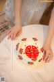 A woman in a white dress holding a white cake with red roses on it.