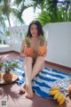 A woman sitting on a towel holding two pineapples.