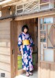 A woman in a blue and pink kimono standing in front of a wooden door.