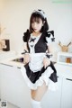 A woman in a maid outfit posing in a kitchen.