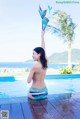 A woman in a bikini sitting on the edge of a swimming pool.