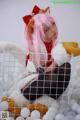 A woman with pink hair sitting in a cage filled with white balls.