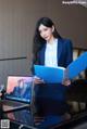 A woman in a blue suit holding a blue folder.