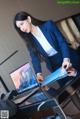 A woman in a blue suit standing next to a laptop computer.