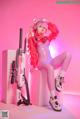 A woman in a pink outfit sitting on a white cube with a gun.