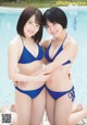 Two women in blue bikinis posing next to a swimming pool.