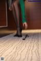 A woman in a green shirt and black stockings standing on a carpet.