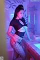 A woman in a black top and fishnet stockings posing in a bathroom.