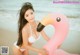 A woman in a white bikini holding a pink flamingo on the beach.