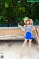 A woman in a blue dress and hat standing next to a boat.