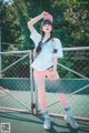 A woman standing on a tennis court wearing pink leggings and a white shirt.