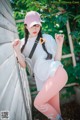 A woman leaning against a wall wearing pink leggings and a baseball cap.