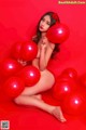 A naked woman sitting on a bed of red balloons.