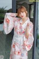 A woman wearing a white kimono standing in front of a window.