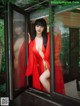 A woman in a red robe is looking out of a window.