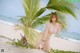 A woman in a bikini posing under a palm tree on the beach.