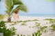 A woman in a bikini sitting under a palm tree on the beach.