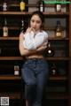 A woman sitting on a stool in front of a shelf of liquor bottles.