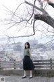 A woman standing in front of a tree with a city in the background.