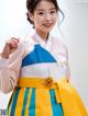 A woman in a blue and yellow hanbok poses for a picture.