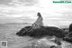 A woman sitting on a rock in the ocean.