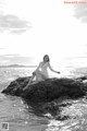 A woman sitting on a rock in the ocean.