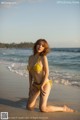 A woman in a yellow bikini sitting on the beach.