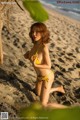 A woman in a yellow bikini sitting on a beach.