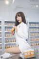 A woman in a lab coat sitting on a counter holding a bottle of pills.