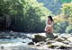 A woman sitting on a rock in the middle of a river.