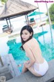 A woman in a white bathing suit sitting by a swimming pool.