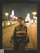 A woman in a kimono standing on a sidewalk at night.