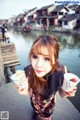 A woman holding two cups of ice cream in front of a river.