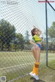 A woman in a green and yellow outfit posing in front of a fence.