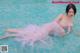 A woman in a pink dress laying on the edge of a pool.