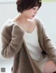 A woman sitting on a window sill wearing a brown cardigan.