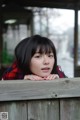 A woman leaning on a wooden fence with her hand on her chin.