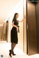 A woman in a black dress standing in an elevator.